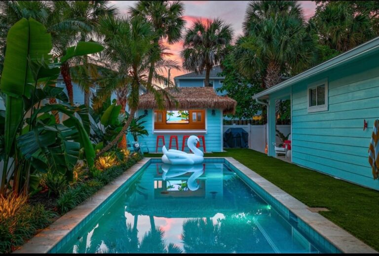 Beautiful backyard pool with tropical plants and a swan float at sunset.